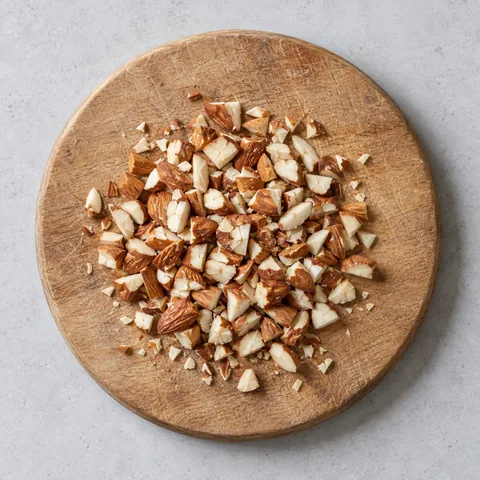 Roughly chopped raw almonds on a wooden cutting board.