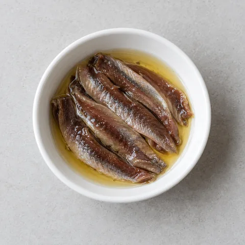 Oil-packed anchovy fillets in a small white bowl.