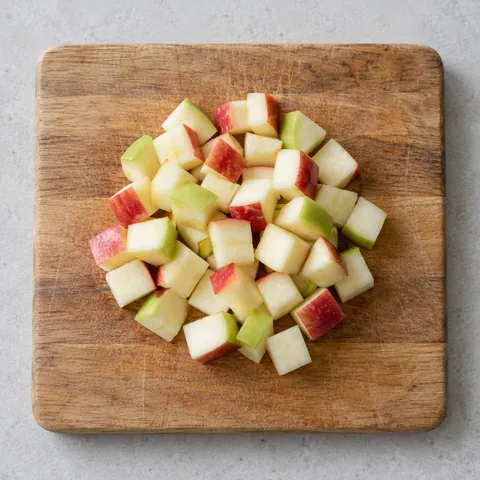 Cored apple cut into half-inch cubes on a wooden cutting board.