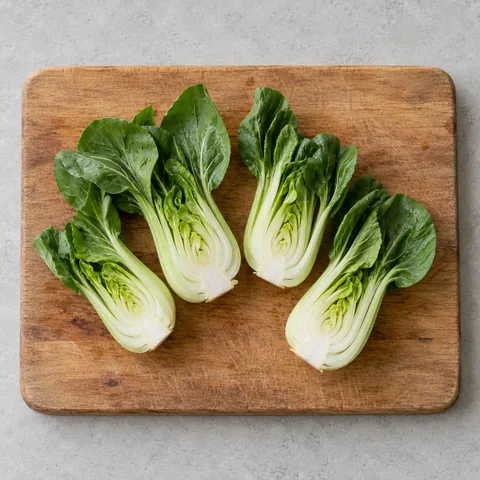 Baby bok choy halved lengthwise on a wooden cutting board.