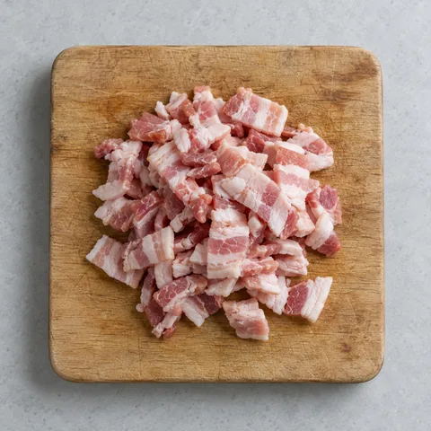 Raw thick-cut bacon cut into half-inch pieces on a wooden cutting board.