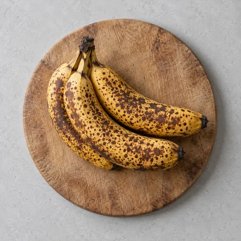 Very ripe bananas with heavily speckled peels on a wooden cutting board.