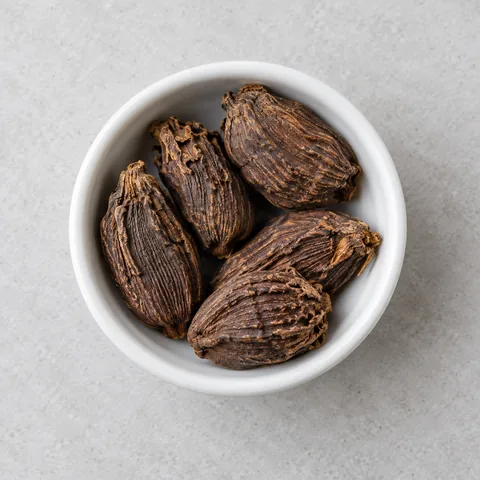 Whole black cardamom pods in a small white ramekin.