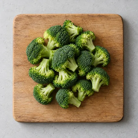 Broccoli cut into bite-size florets on a wooden cutting board.