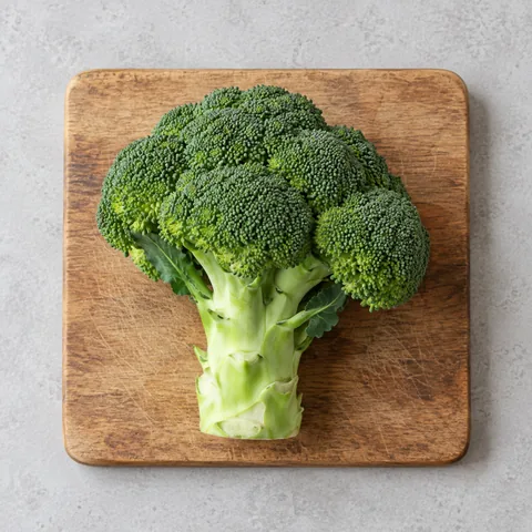 A whole head of broccoli with its stem on a wooden cutting board.