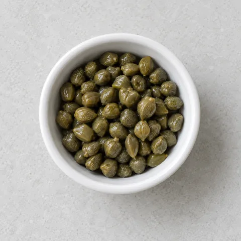 Drained capers in a small white ramekin.
