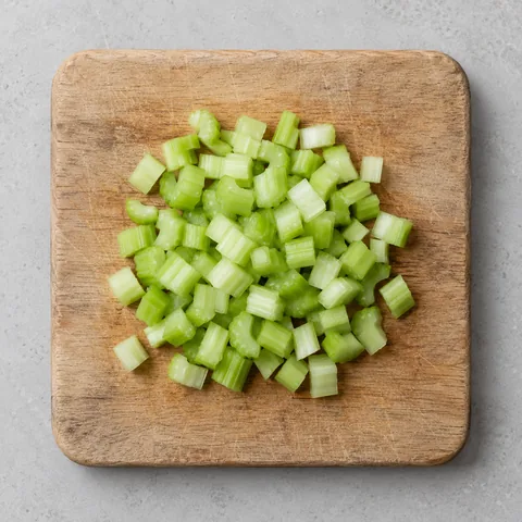Celery cut into small dice on a wooden cutting board.