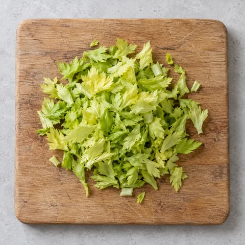 Chopped pale inner celery leaves on a wooden cutting board.
