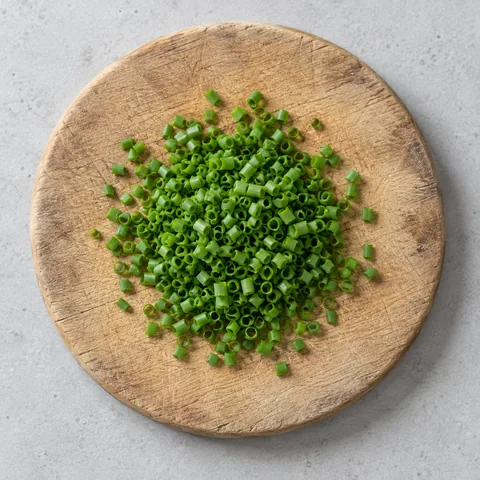 Finely chopped fresh chives on a wooden cutting board.