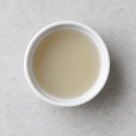 Bottled clam juice in a small white ramekin.