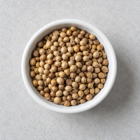 Whole coriander seeds in a small white ramekin.