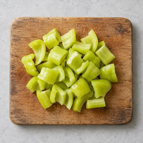 Seeded Cubanelle pepper cut into chunks on a wooden cutting board.