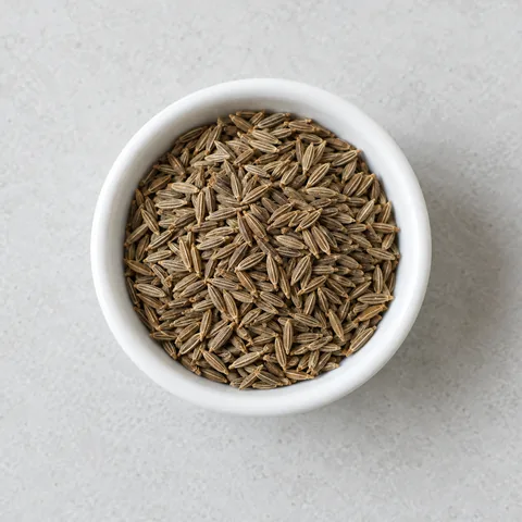 Whole cumin seeds in a small white ramekin.