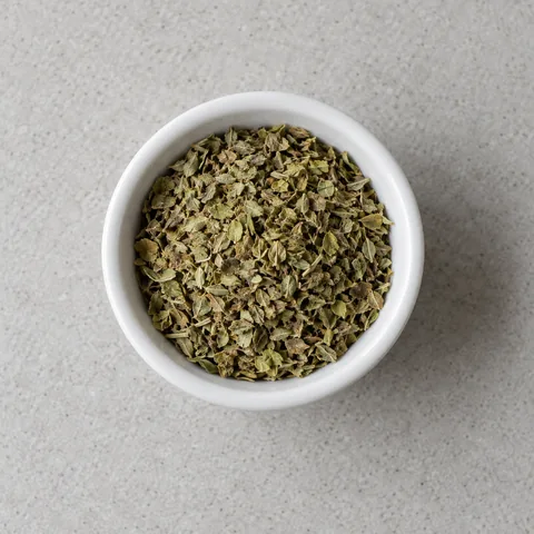 Dried oregano leaves in a small white bowl.