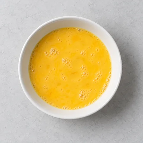 Beaten eggs in a small white bowl.