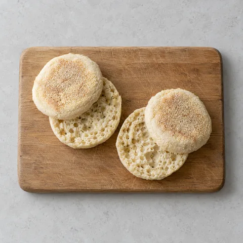 English muffins split in half on a wooden cutting board.