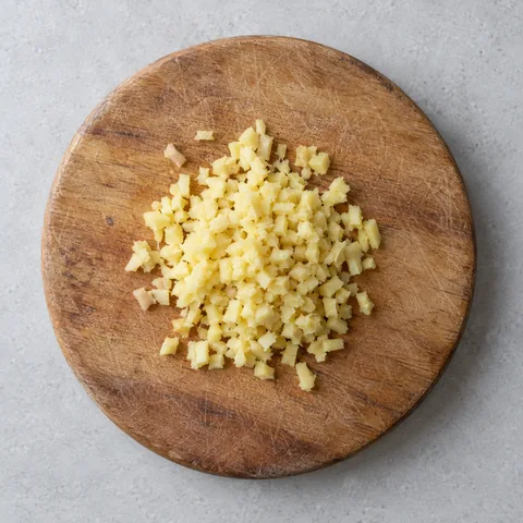 Minced peeled fresh ginger on a wooden cutting board.