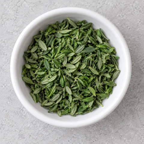 Fresh thyme leaves stripped from the stems in a small white ramekin.
