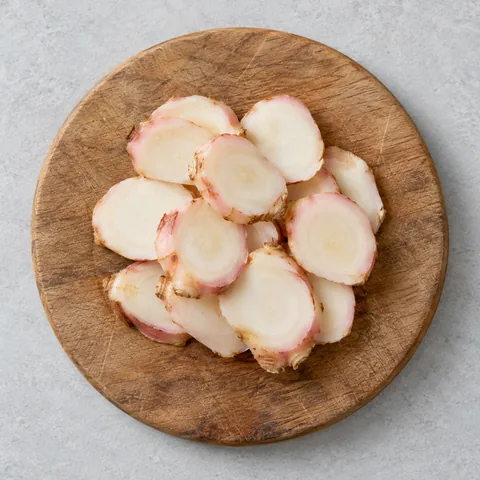 Fresh galangal cut into thin coins on a wooden cutting board.