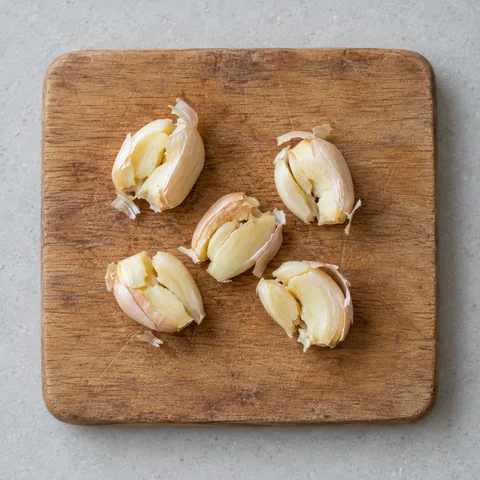 Lightly smashed garlic cloves on a wooden cutting board.