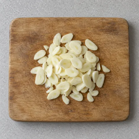 Thin slices of raw garlic on a cutting board.