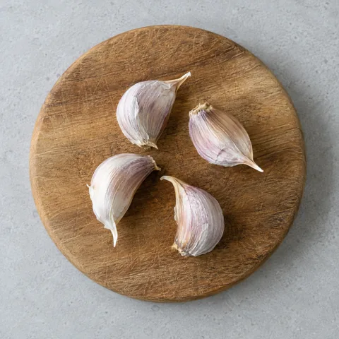 Unpeeled garlic cloves on a wooden cutting board.