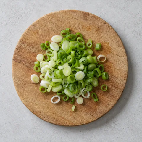 Thinly sliced green onions on a wooden cutting board.