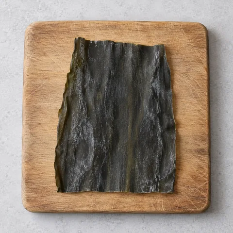 A dried kombu piece on a wooden cutting board.