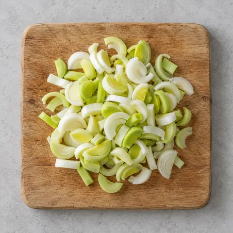Leeks halved and sliced into half-moons on a wooden cutting board.