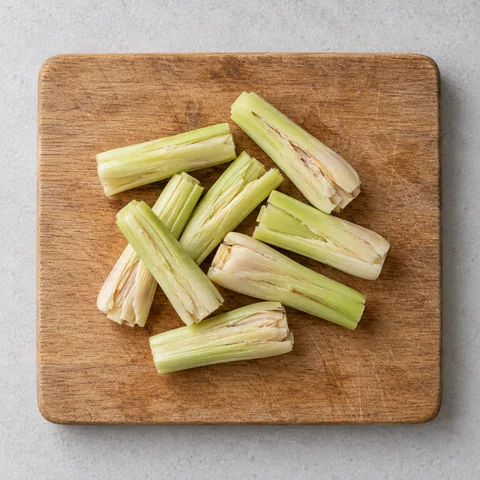 Lemongrass cut into 2-inch lengths and bruised on a wooden cutting board.