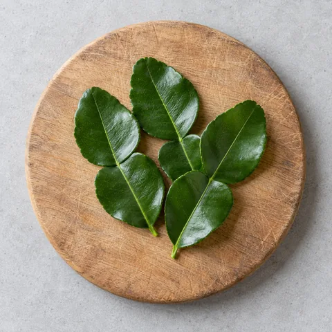 Makrut lime leaves on a wooden cutting board.