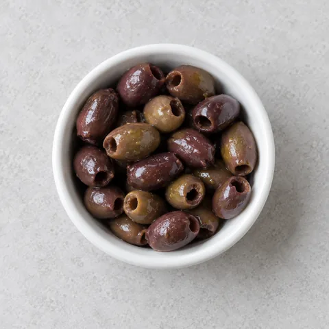 Pitted small Nicoise olives in a small white ramekin.