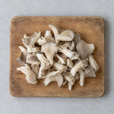 Oyster mushrooms torn into bite-size pieces on a wooden cutting board.