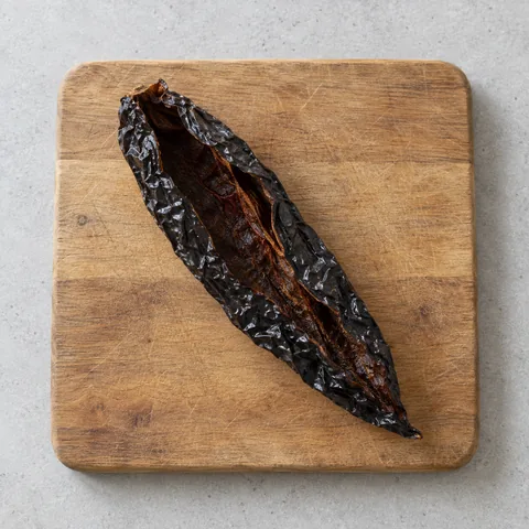 Dried pasilla chile, stemmed and seeded on a wooden cutting board.