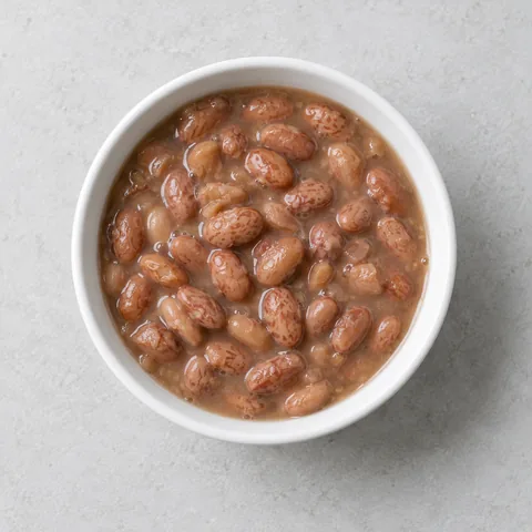 Canned pinto beans in their liquid in a small white bowl.