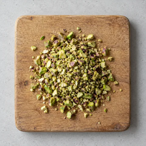 Chopped pistachios on a wooden cutting board.