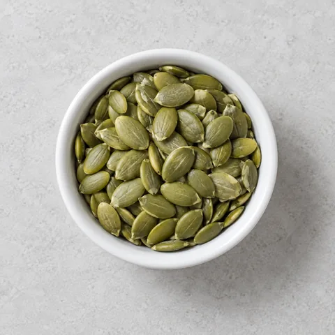 Raw hulled pumpkin seeds (pepitas) in a small white ramekin.