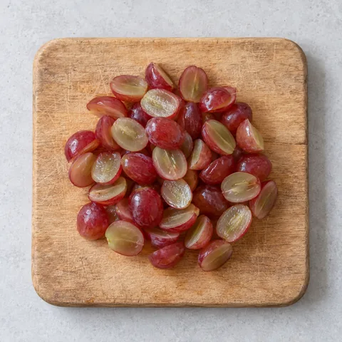 Seedless red grapes, halved on a wooden cutting board.