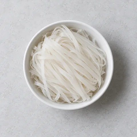 Dried flat rice noodles in a small white bowl.