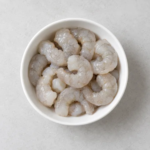 Raw shrimp, peeled and deveined in a small white bowl.