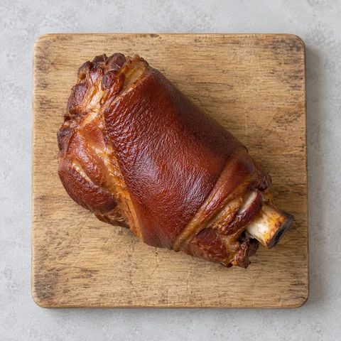 A meaty smoked ham hock on a wooden cutting board.