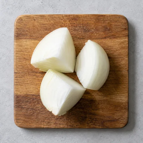 White onion cut into large thick pieces on a wooden cutting board.