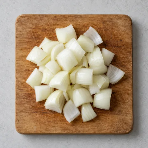 Yellow onion cut into one-inch pieces on a wooden cutting board.