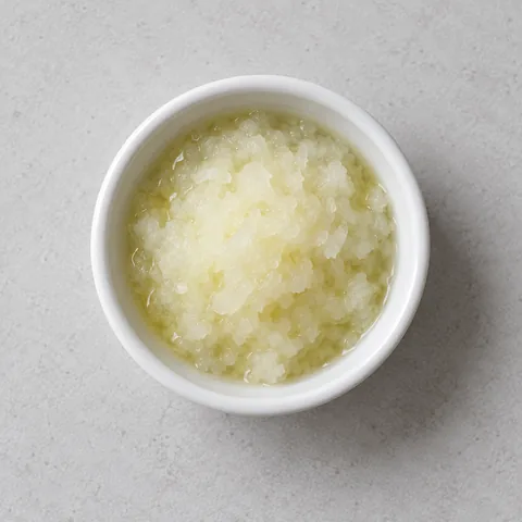 Finely grated yellow onion with its juice in a small white ramekin.