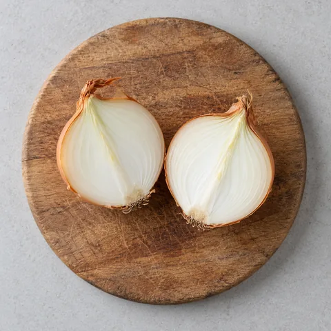 An unpeeled yellow onion halved through the root on a wooden cutting board.