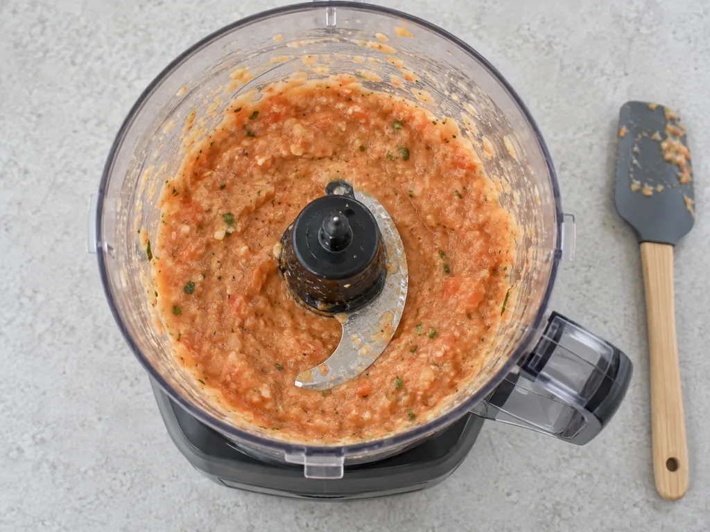 A fairly smooth orange vegetable paste surrounds the blade inside the open food processor.