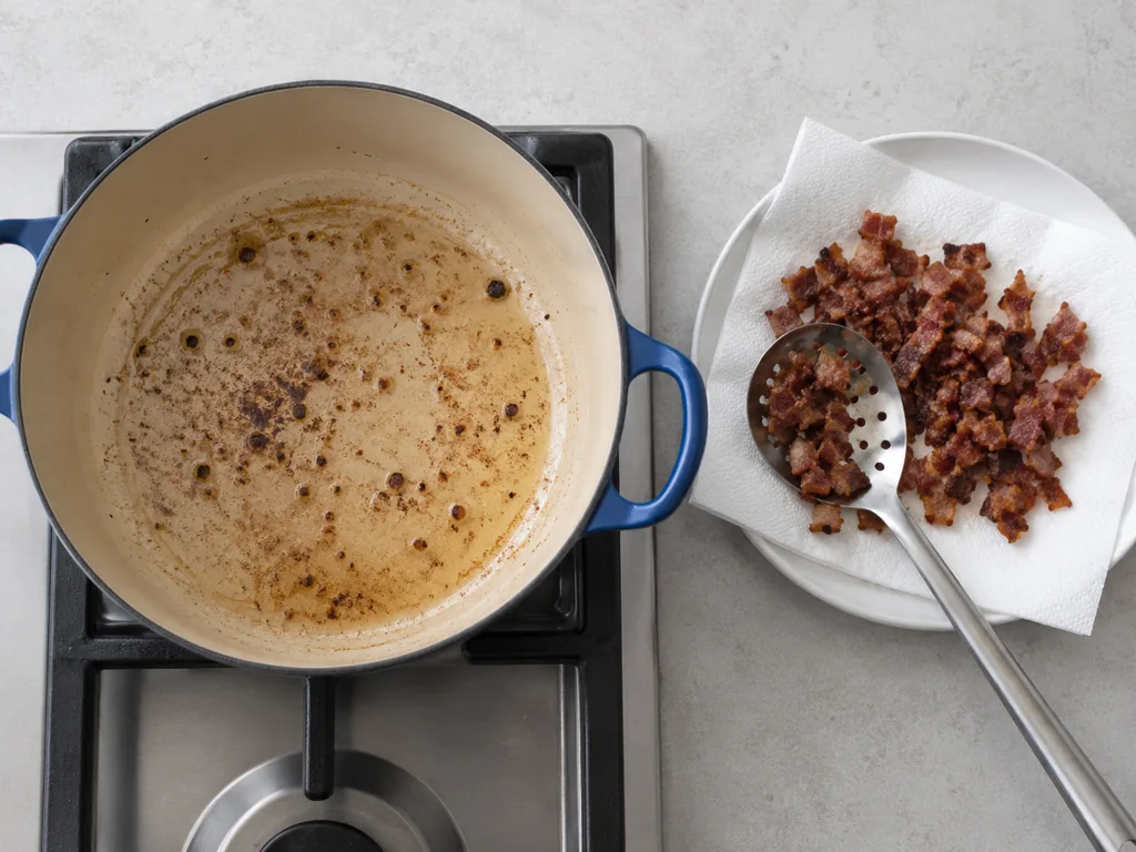 Crisp bacon drains on paper towels beside a pot coated with rendered fat.