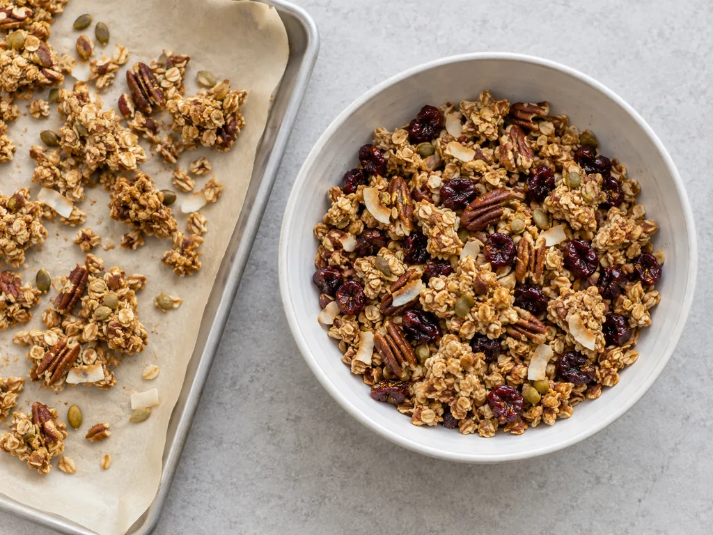 Golden granola clusters mixed with dried cherries fill a bowl beside broken pieces on parchment.
