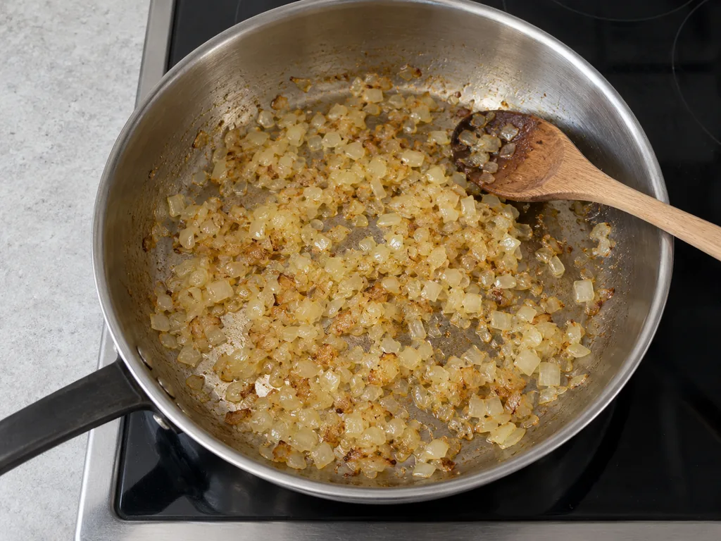 Finely chopped onion softened with lightly golden edges in a skillet.